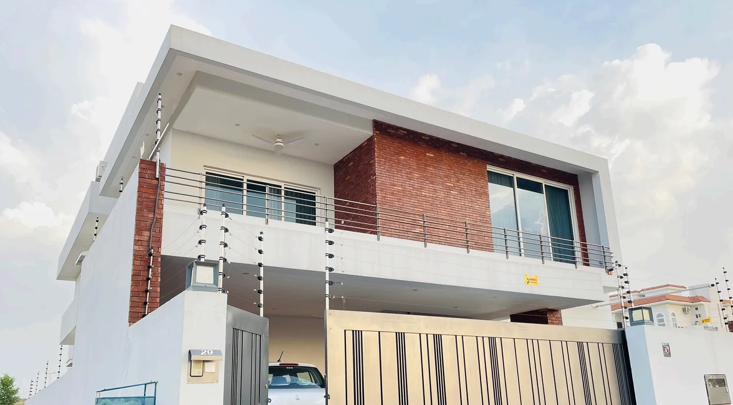 Modern 1 Kanal house exterior in DHA 5 Islamabad featuring exposed red brickwork and minimalist white cubic design by Babar Malik Architects.