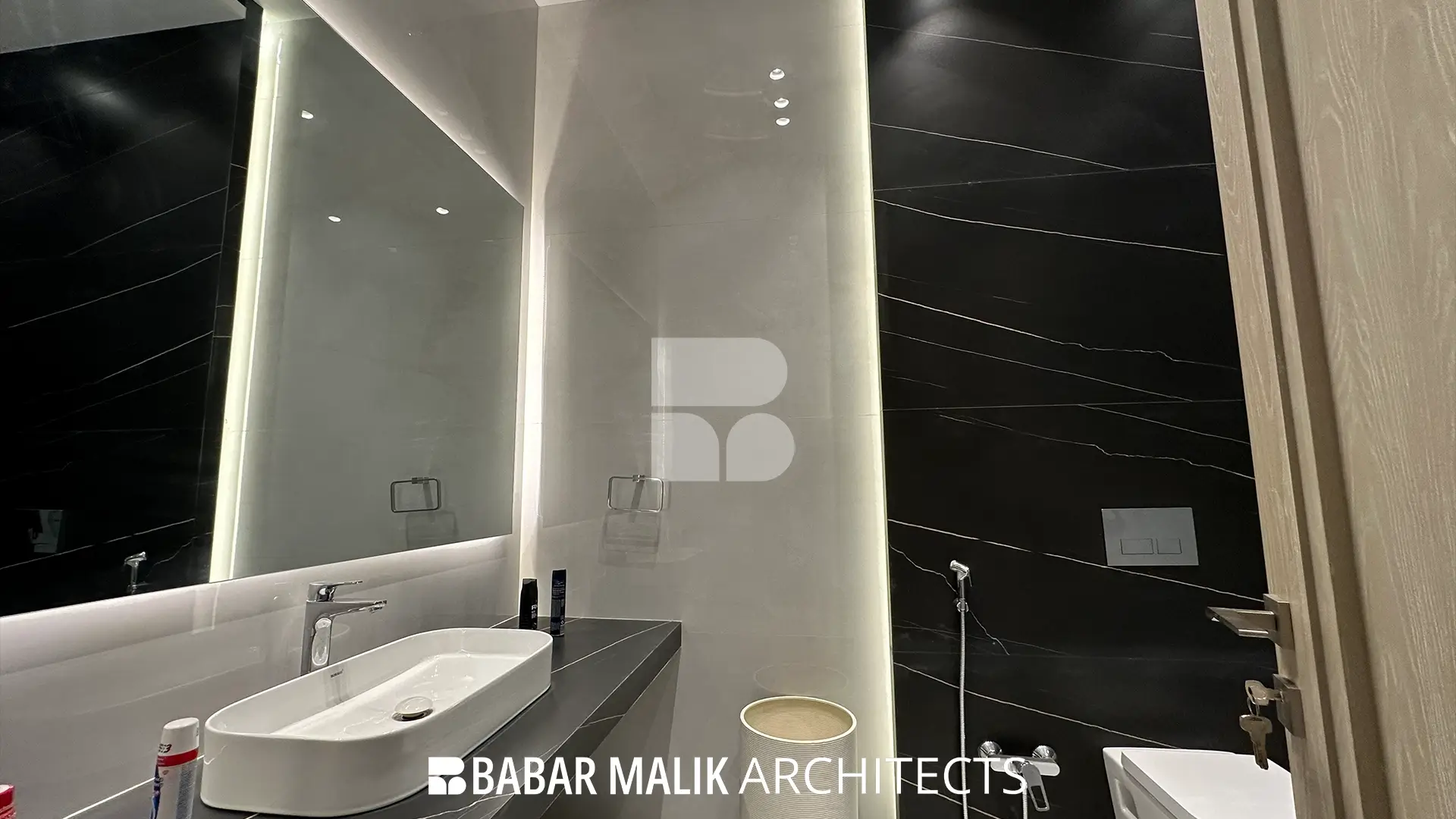 Detailed view of the bathroom vanity showing the white vessel sink, dark countertop, and backlit mirror, alongside a wall-mounted toilet and black accent wall.