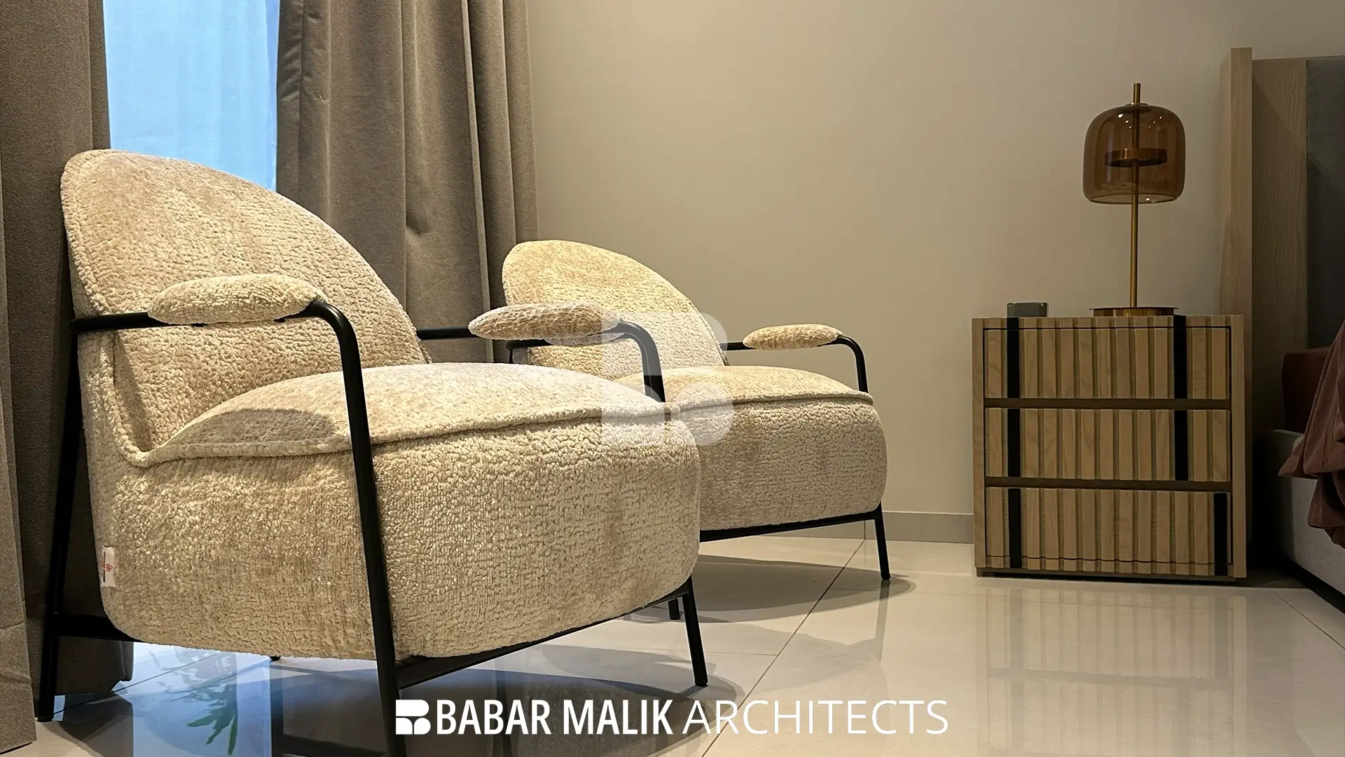 Close-up of two textured bouclé accent chairs with black metal frames situated in the bedroom lounge area.