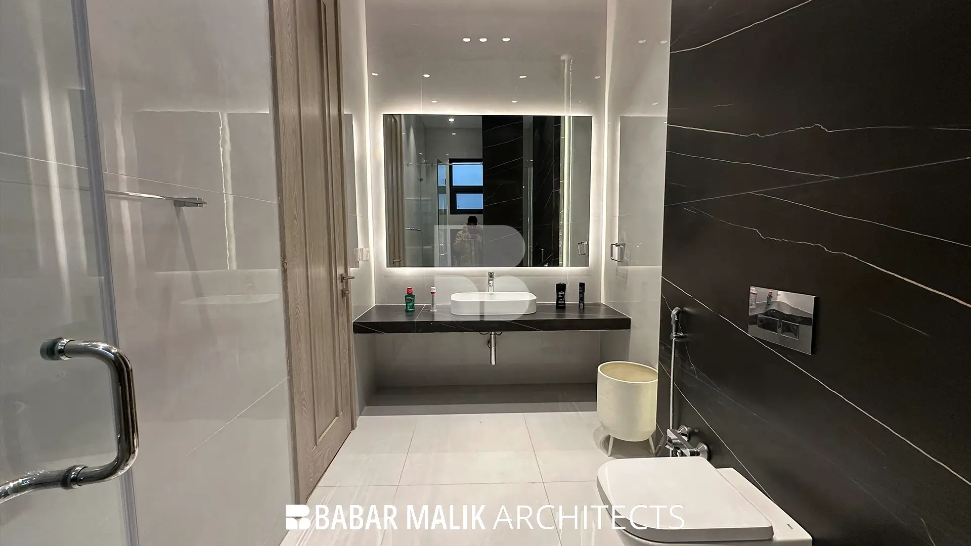 Contemporary bathroom interior utilizing a high-contrast palette with black marble-effect accent tiles, a glass shower enclosure, floating vanity, and wall-mounted plumbing fixtures.