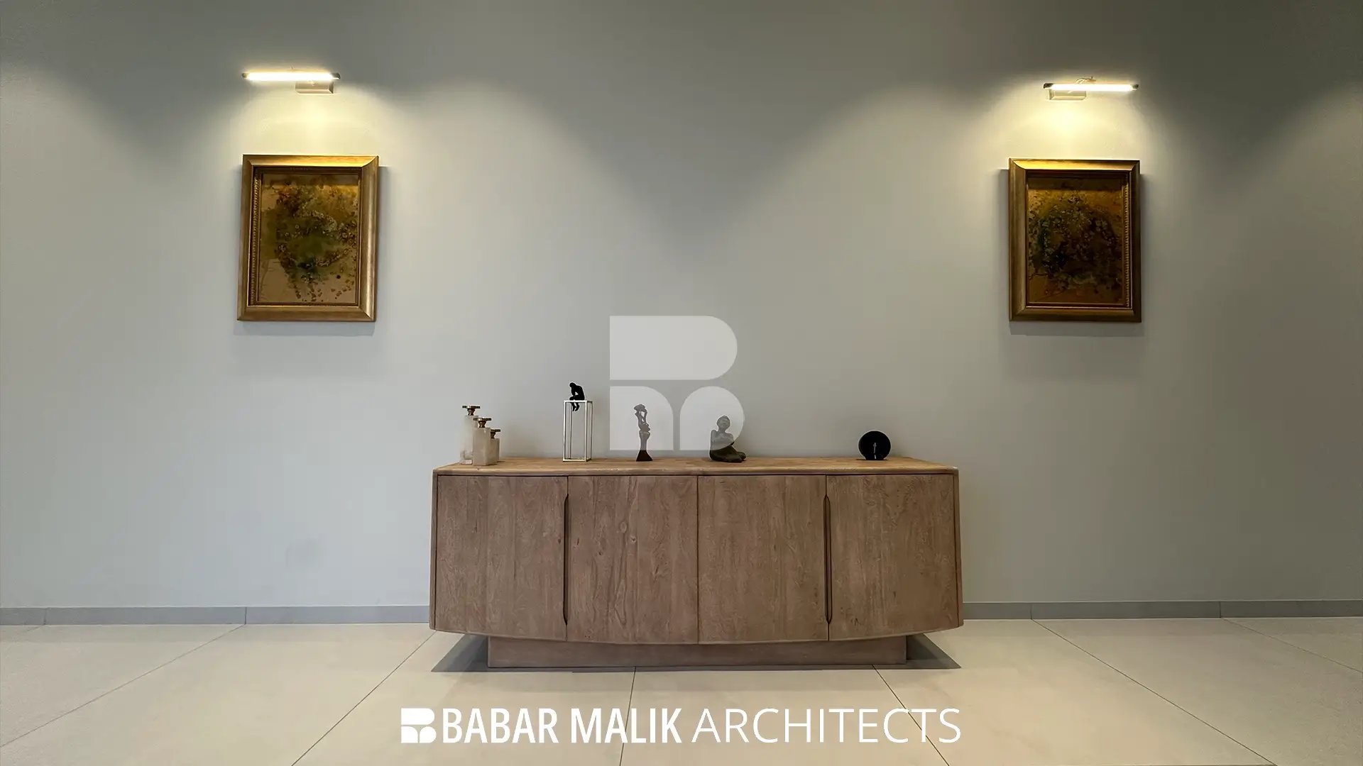 A light-toned, fluted wood credenza placed in a hallway, styled with minimal sculptures and flanked by two small framed artworks illuminated by picture lights.