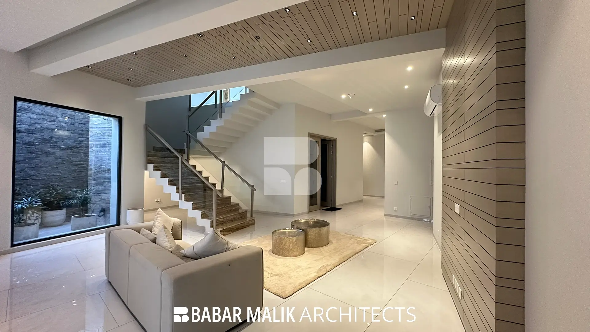 Living room interior with a light color palette, featuring a beige sofa, two cylindrical metallic coffee tables, and a wooden slatted ceiling that extends down the accent wall.