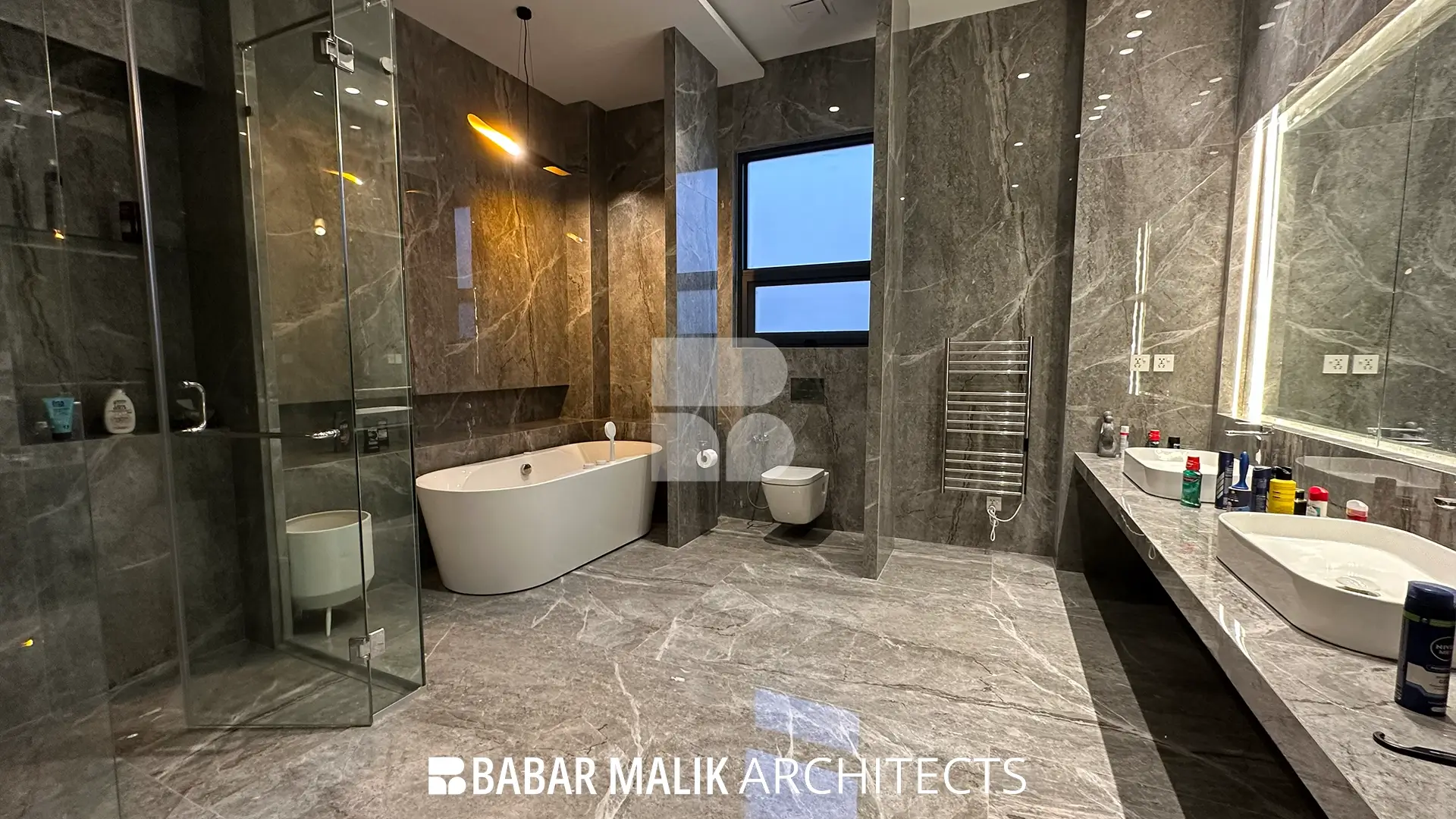 View of the master bathroom highlighting the dual vanity setup with white sinks, an expansive mirror with integrated lighting, and the adjacent freestanding bathtub.