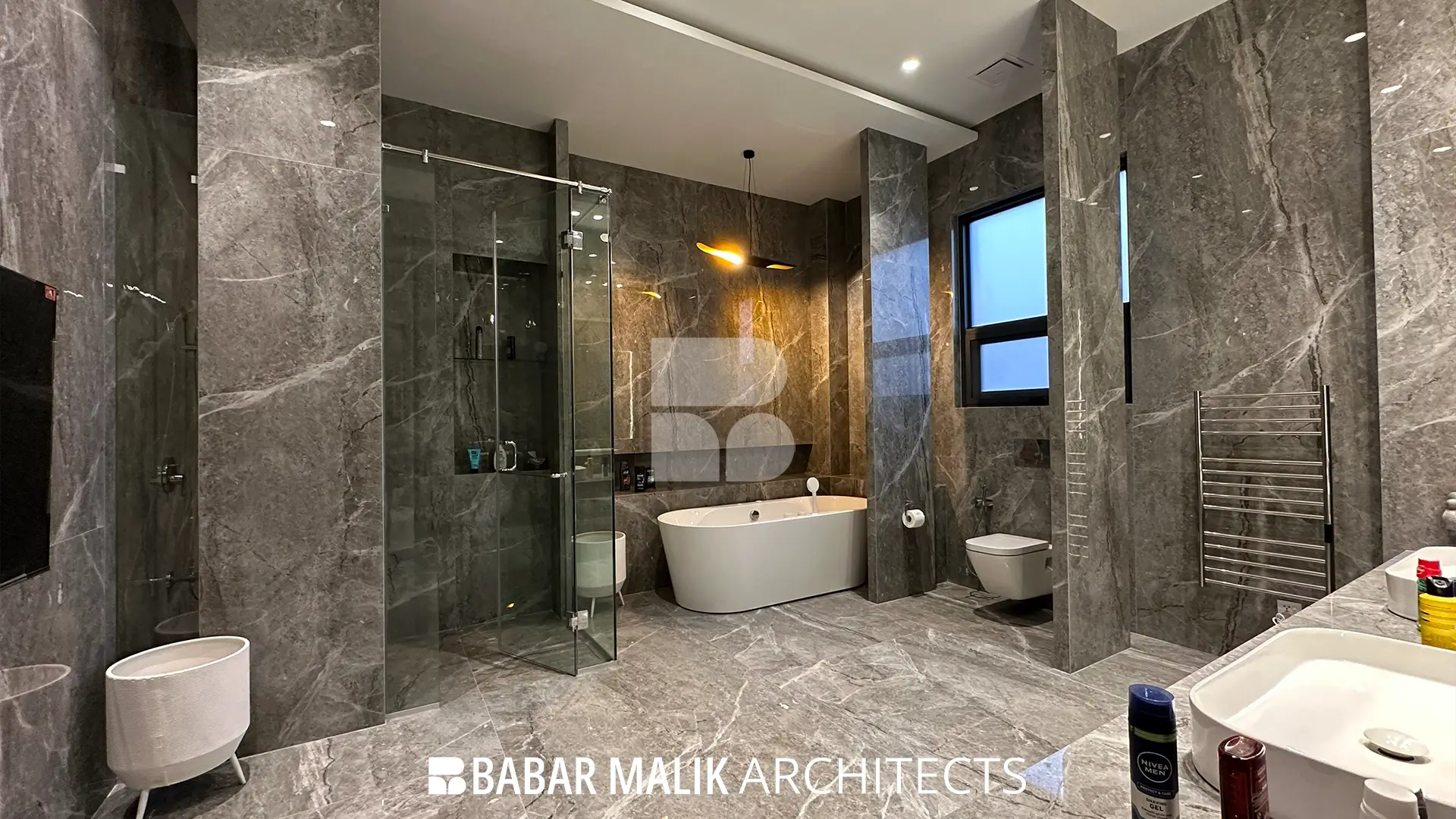Spacious master bathroom clad entirely in grey marble tiles, featuring a freestanding white bathtub, a walk-in glass shower enclosure, and a floating toilet.