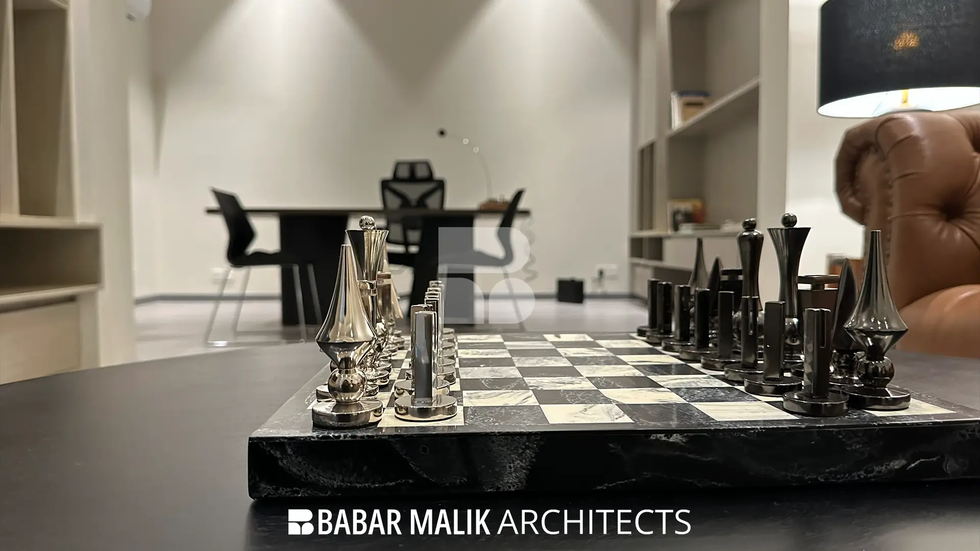 Decorative metallic chess set on a black and white marble board, placed on a dark coffee table with a home office setup blurred in the background.