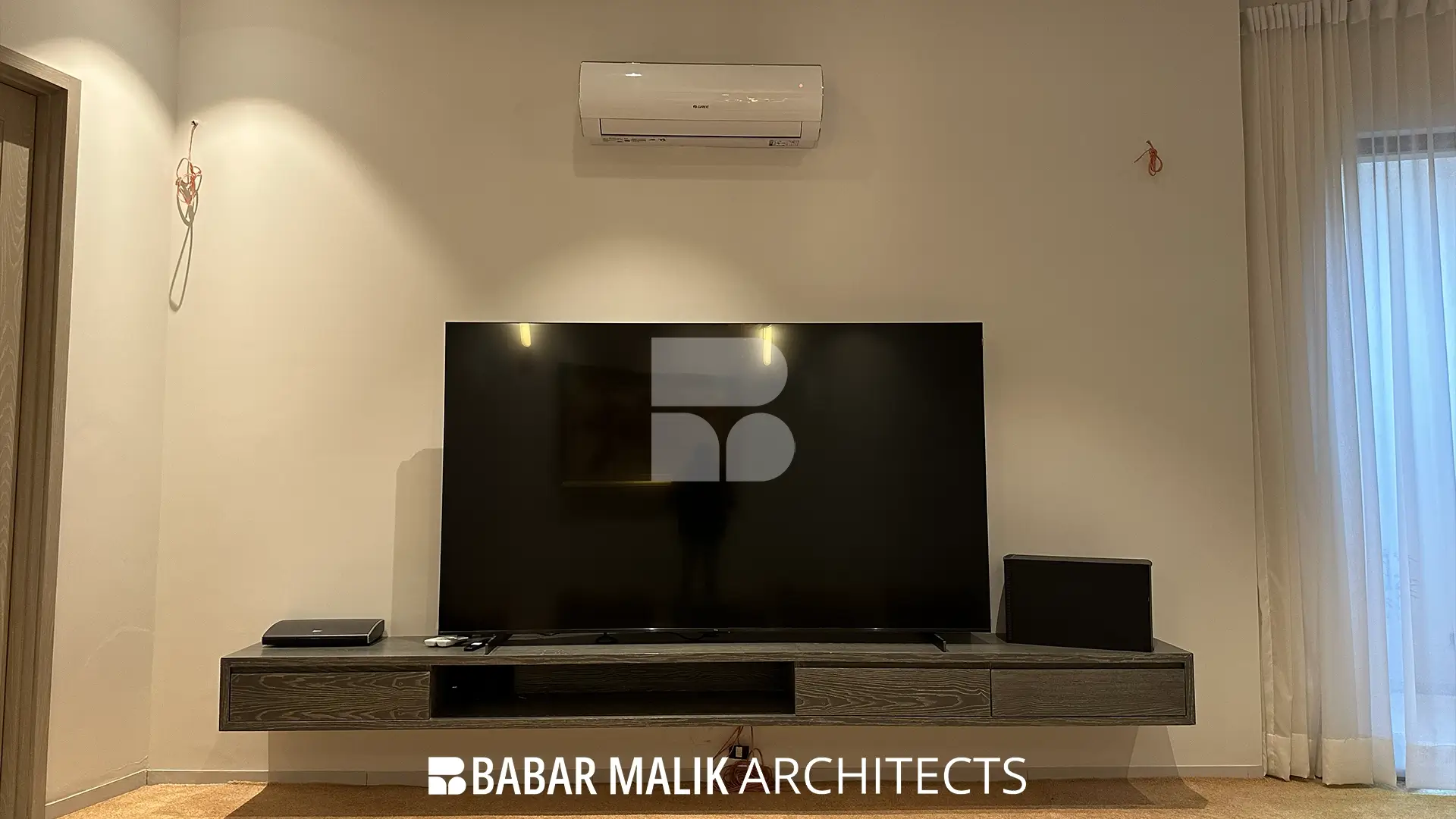 A minimalist entertainment area featuring a large flat-screen television resting on a floating dark wood console against a plain white wall.
