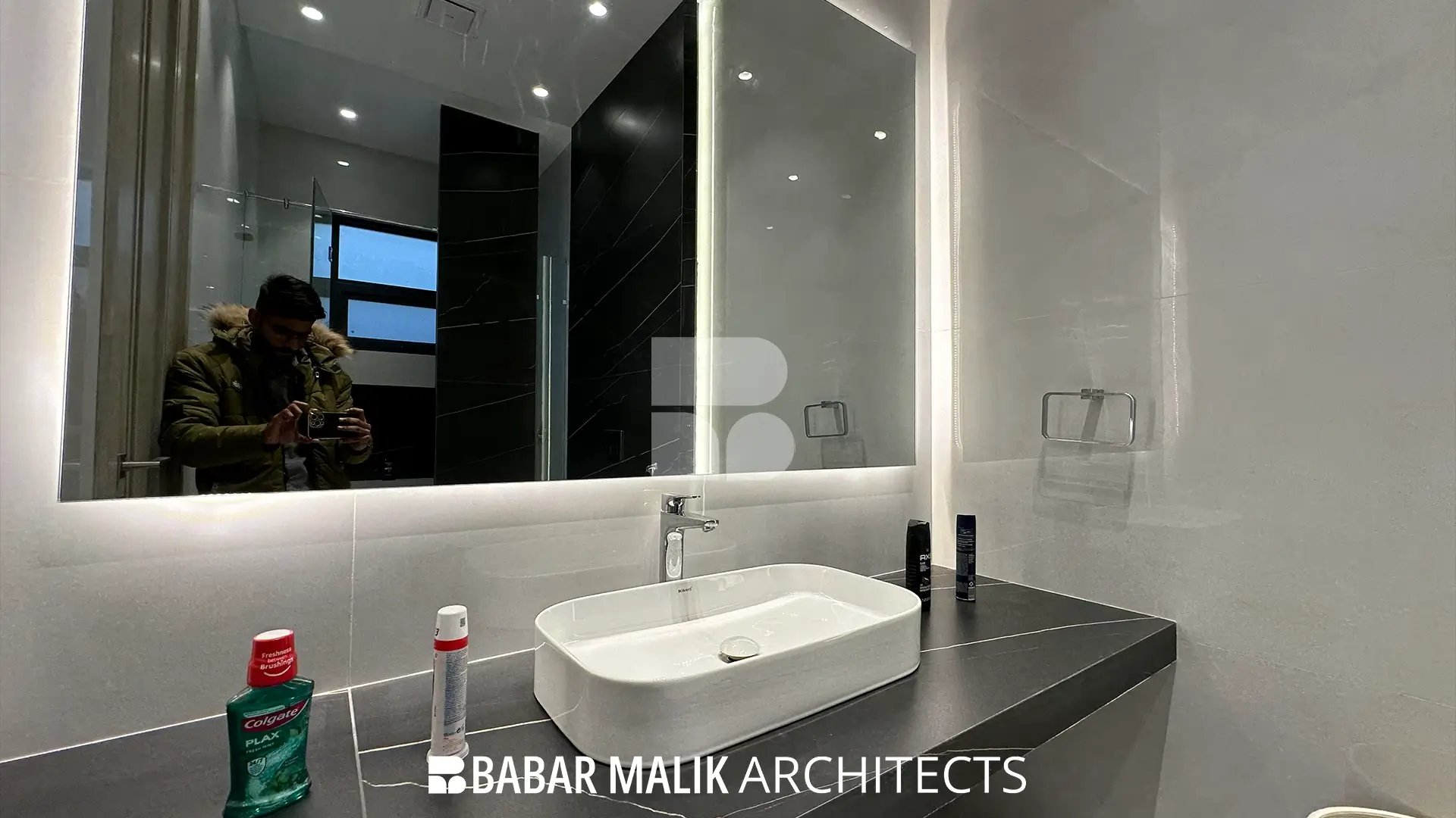 Modern bathroom vanity area featuring a dark countertop, a white rectangular vessel sink, and a large backlit mirror against a dual-toned black and white wall.